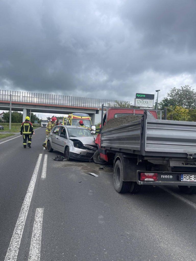 Wypadek na drodze, dwa samochody po zderzeniu, obok stoi strażak, w tle wiaduk