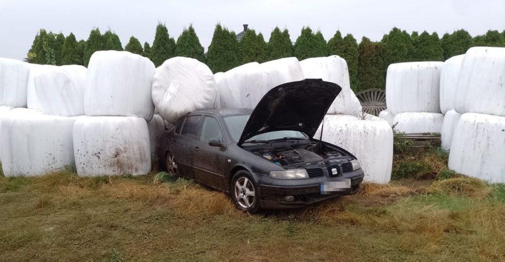 Samochód z uniesioną maską silnika, obok białe bele kiszonki