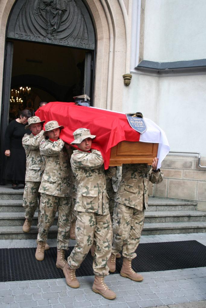 Zołnierze wynoszą trumnę z ciałem poległego kolegi przykrytą białoczerwoną flagą