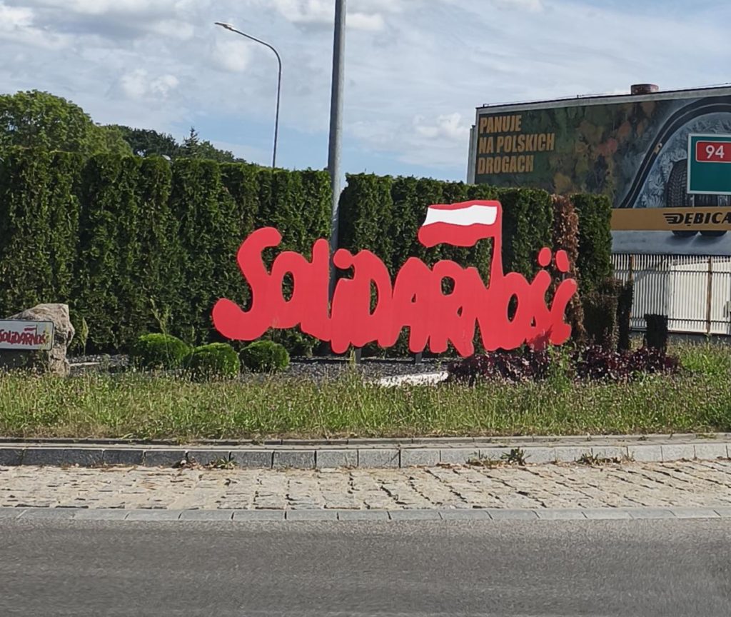 Napis Solidarność na tle zielonego szpaleu krzewów