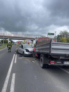 Wypadek na drodze, dwa samochody po zderzeniu, obok stoi strażak, w tle wiaduk