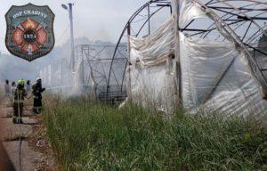 Strażak w stroju bojowym gasi pożar trawy i folii na tunelu ogrodniczym