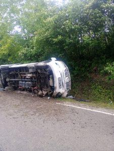 Biały autobus leży przewrócony na boku drogi