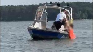 Policyjna łódka na jeziorze wyciąga kobietę w długiej czerwonej sukni z wody