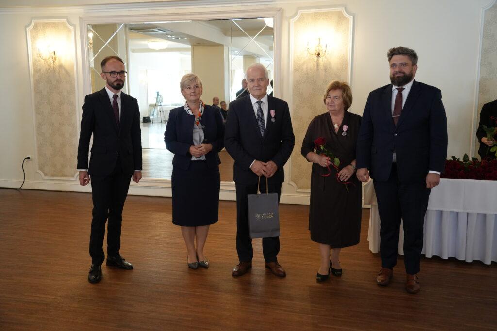 pięć osóbu w uroczystych strojach w przystrojonej sali