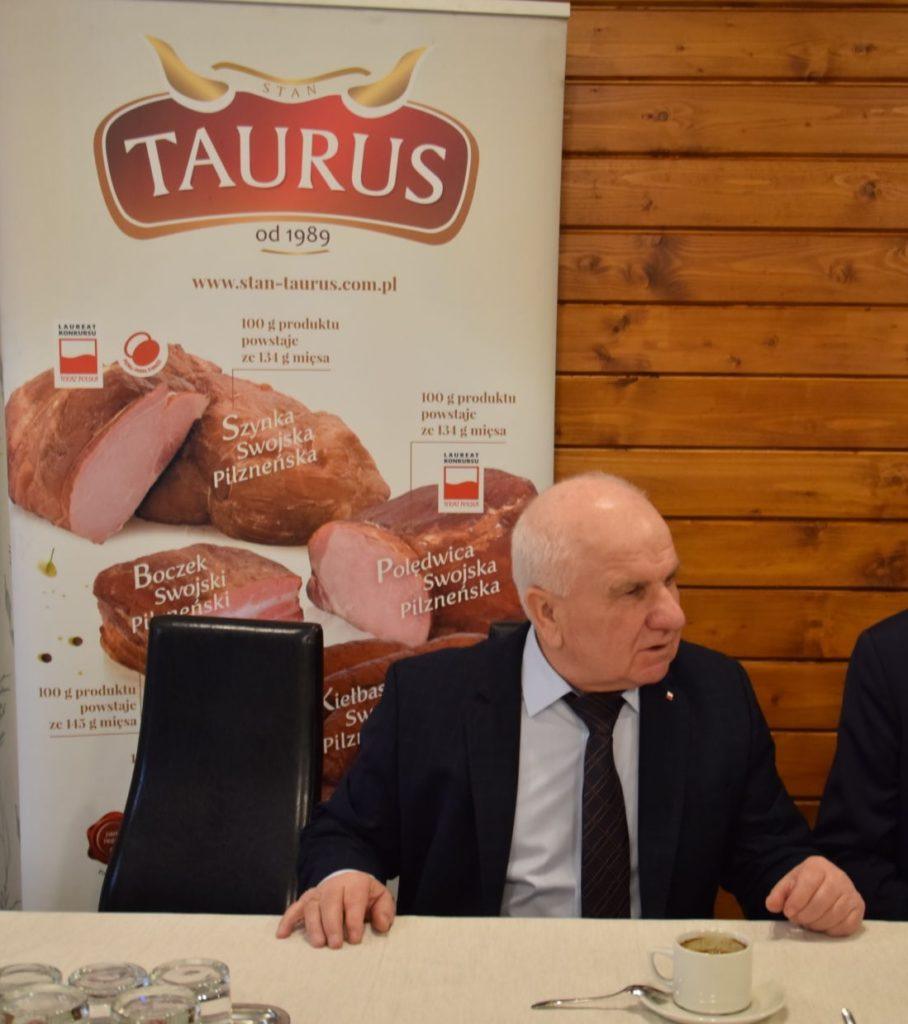 Prezes Stanisław Jarosz na tle plakaru z wyrobami firmy Taurus