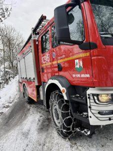Czerwony wóz strażacki, zaśnieżona droga, na kołach łańcuchy śniegowe