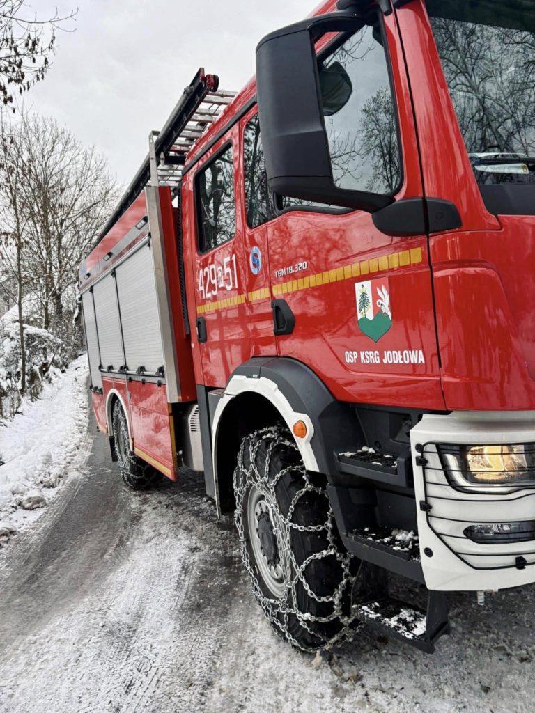 Czerwony wóz strażacki, zaśnieżona droga, na kołach łańcuchy śniegowe