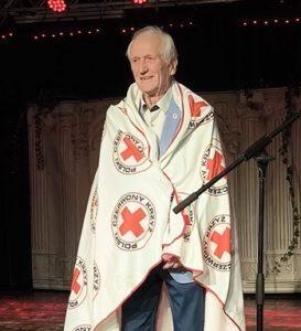 starszy mężczyna otulony białym kocem z logo pck