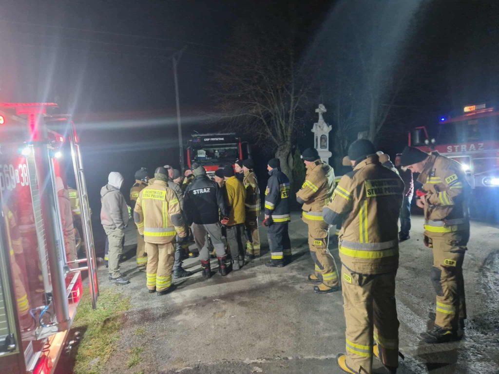 Noc, grupa strażaków, z boku światła reflektorów