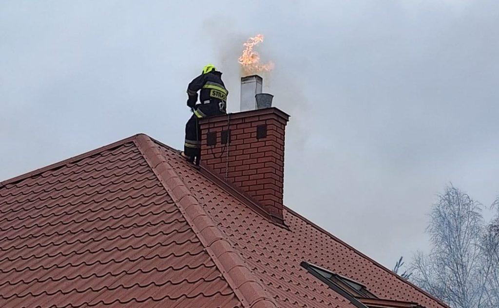 Strażak gasi pożar sadzy w kominie na dachu budynku mieszkalnego w powiecie dębickim