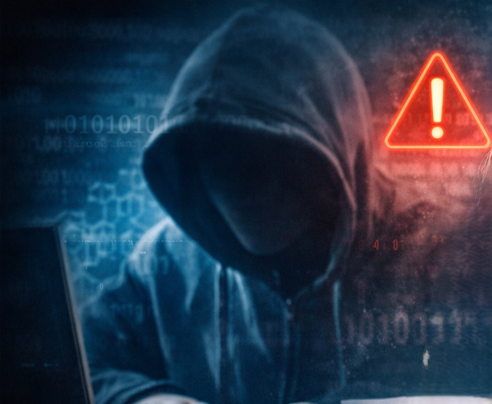 Zakapturzona postać siedząca nad laptopem