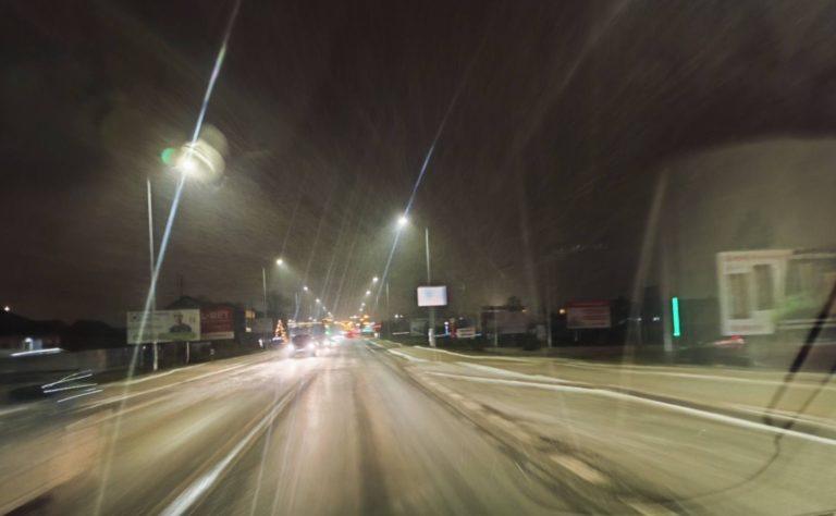 Nocna ulica w powiecie dębickim, delikatnie ośnieżona, przy silnym mrozie. Śnieg opada w świetle latarni i reflektorów miasta, tworząc magiczną, zimową atmosferę.