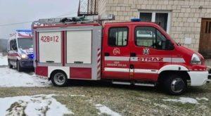 Czerwony wóz strażacki, obok karetka pogotowia na tle domu.