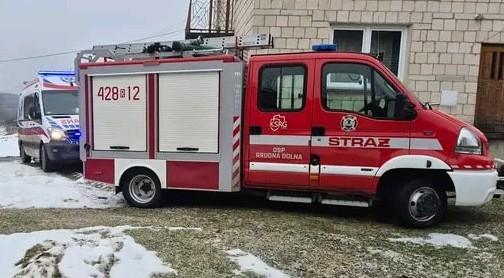 Czerwony wóz strażacki, obok karetka pogotowia na tle domu.