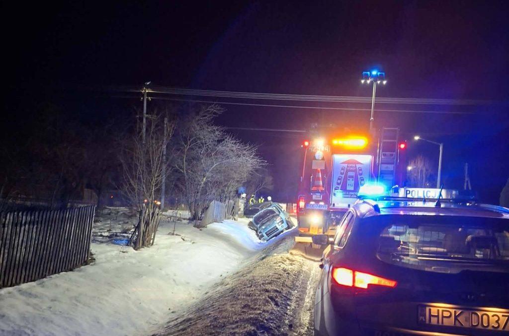 Zimowy wypadek drogowy w Starej Jastrząbce – samochód w rowie przy zaśnieżonej drodze, na miejscu straż pożarna, policja i służby ratunkowe