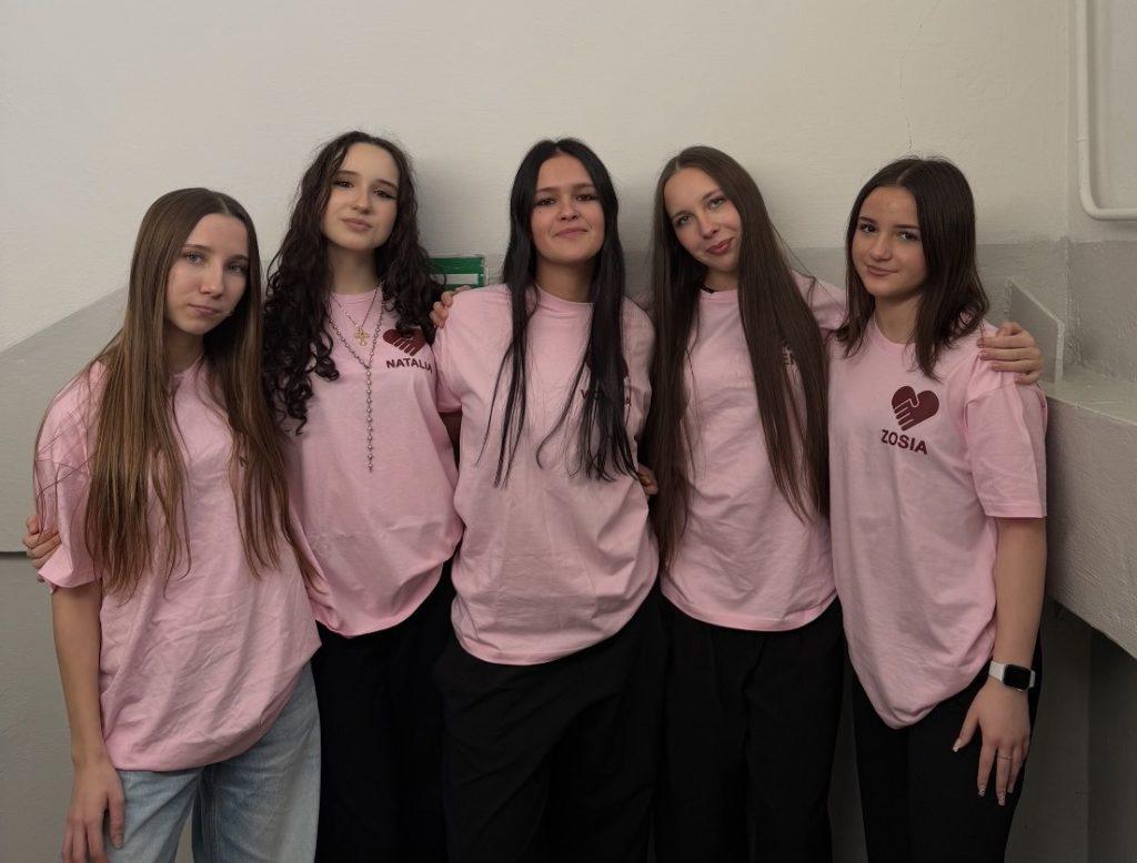 Pięć nastolatek w różowych bluzach uczestniczy w projekcie społecznym Open Hearts w Dębicy, promując empatię i integrację międzypokoleniową