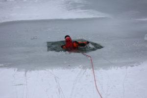 Zaśnieżony staw, przerębla w lodzie, w niej człowiek w czerwonym stroju