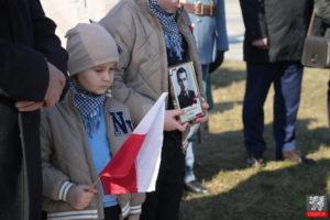 dwoje dzieci z biało czerwoną falgą u zdjęciem żołnierza